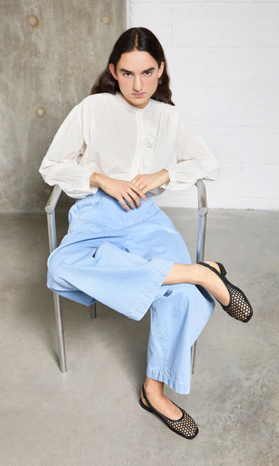 Plümo- Person sitting on a metal chair in Noa Slingbacks, white blouse, and light blue jeans, looking at the camera.