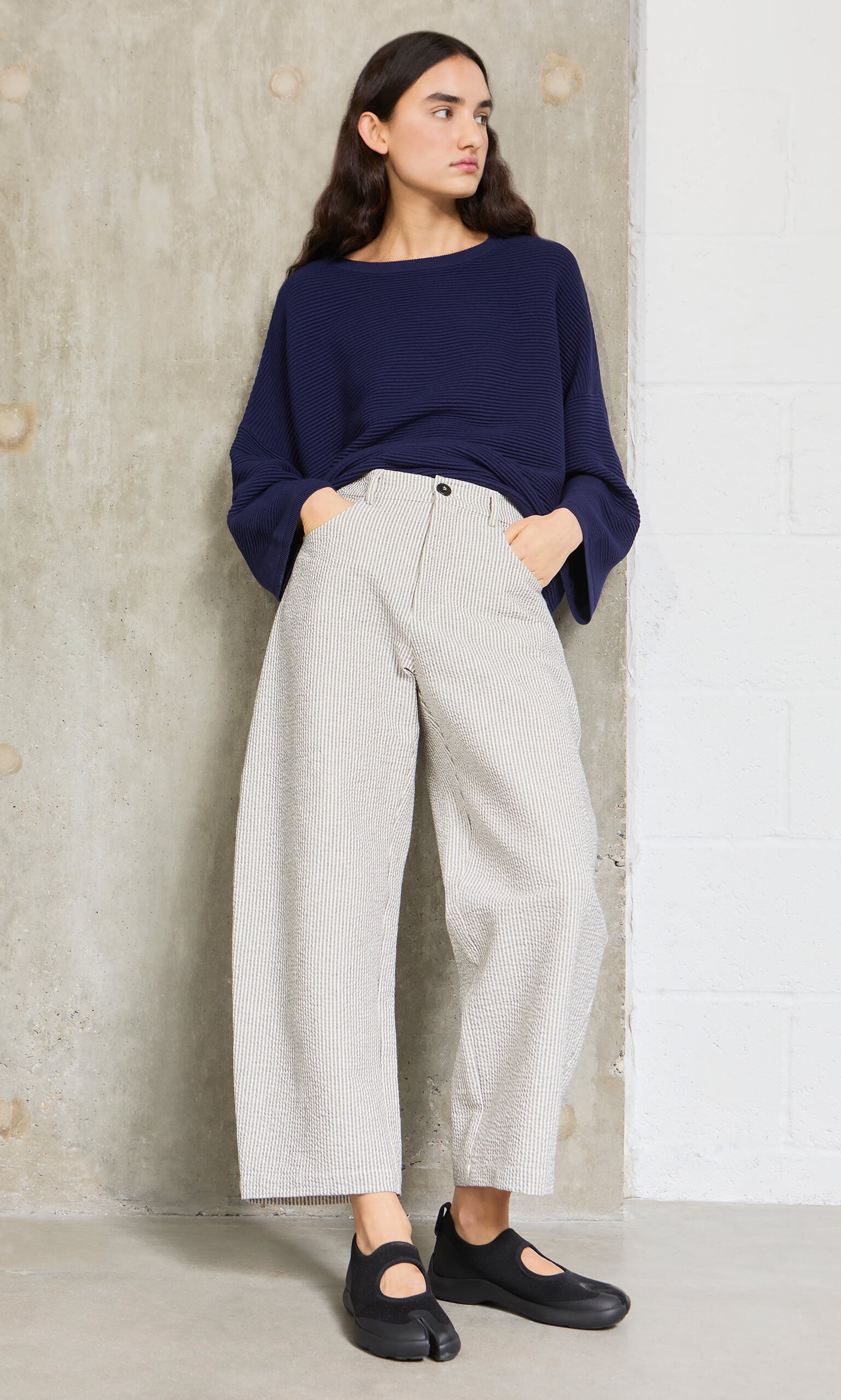 Plümo- Woman in a navy top and Passanti Pants stands against a concrete wall, wearing black shoes.