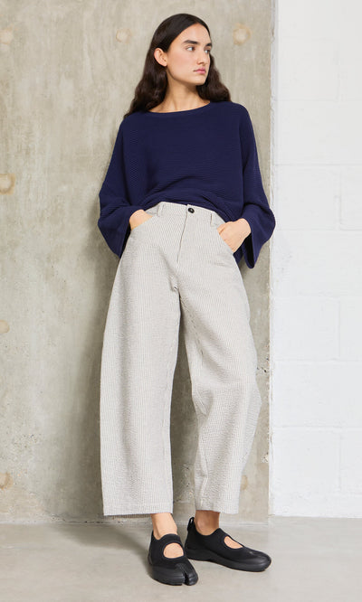 Plümo- Woman in a navy top and Passanti Pants stands against a concrete wall, wearing black shoes.