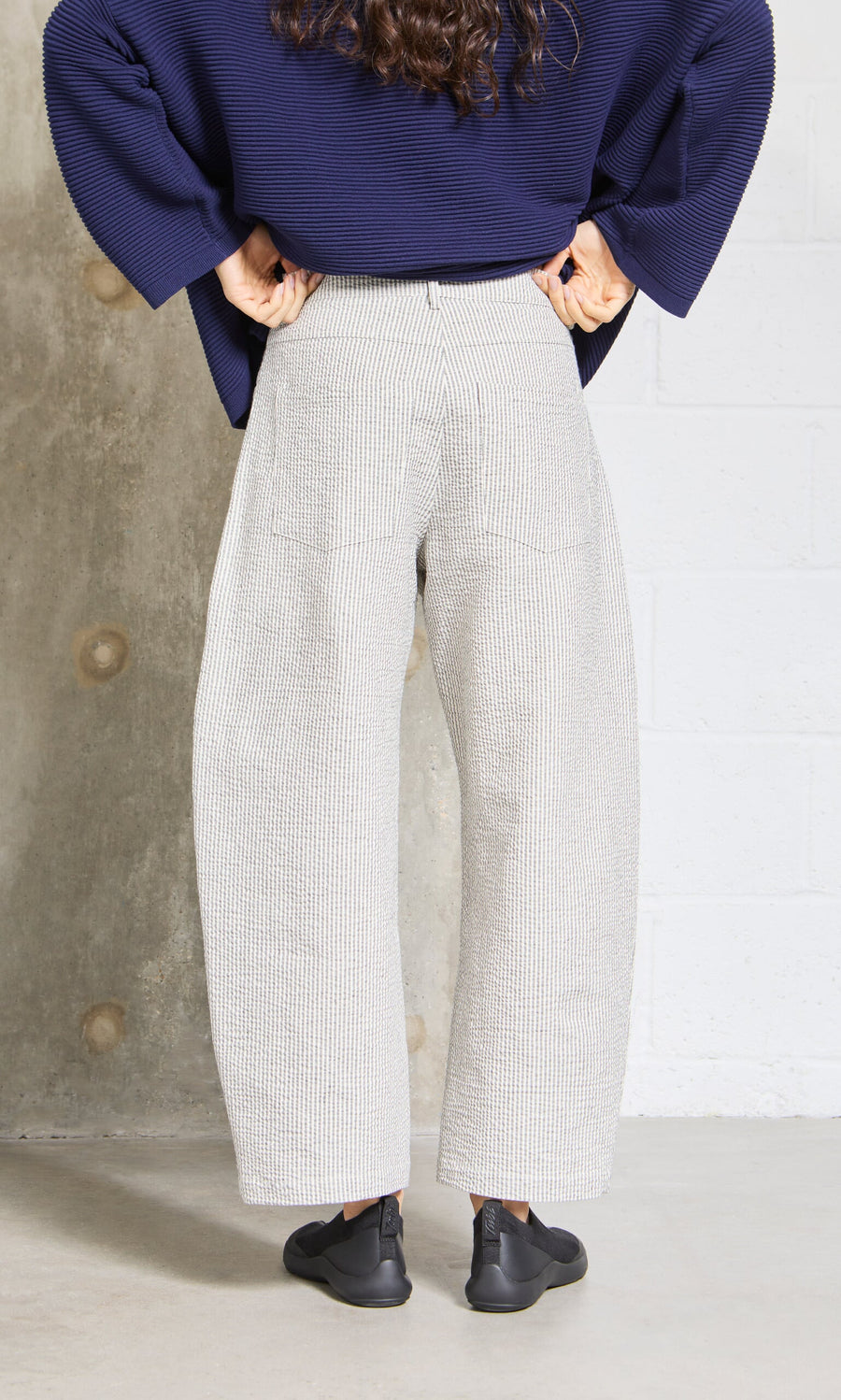 Plümo- Person stands with hands on hips, wearing Passanti Pants, navy top, and black shoes, facing away from the camera.