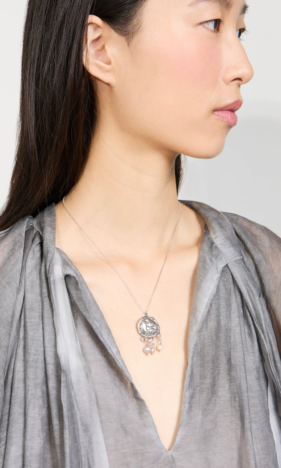 Plümo- Woman in a sheer gray blouse wears the Pearled Necklace, a sterling silver pendant with dangling details.