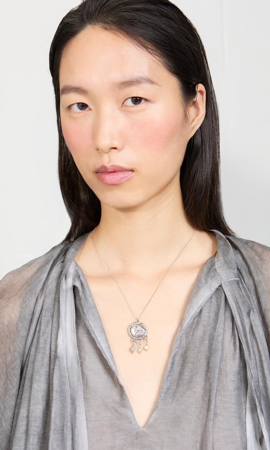 Plümo- A woman in a sheer gray top wears the Pearled Necklace, looking directly at the camera.