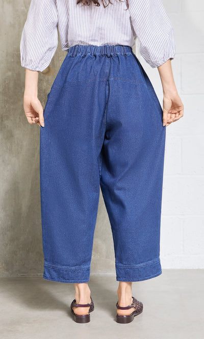 Plümo- Person wearing Polder Pants - Original Denim with elastic waist, sandals, facing away against a concrete wall.