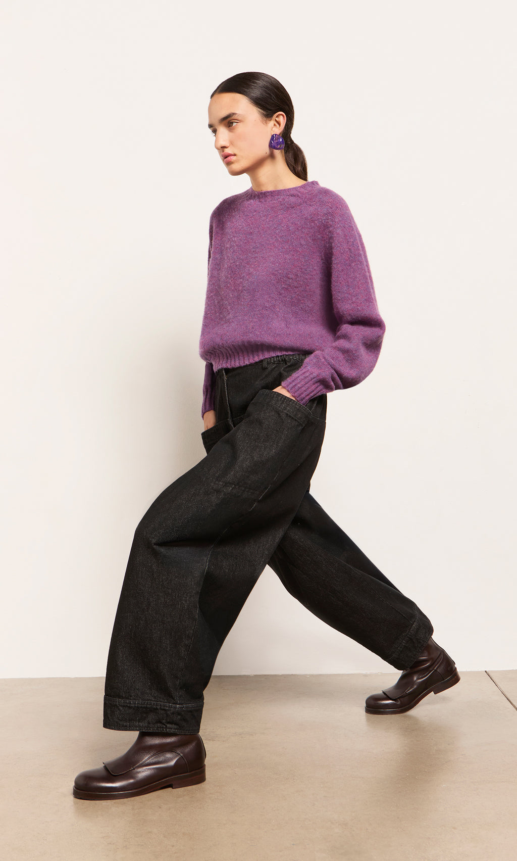 Plümo  Woman in a Wicklow Crewneck - Heather, black wide-leg pants, and brown loafers walks against a plain background.