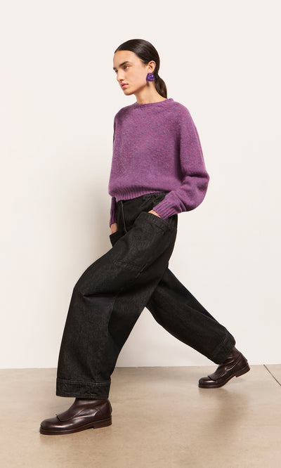 Plümo  Woman in a Wicklow Crewneck - Heather, black wide-leg pants, and brown loafers walks against a plain background.