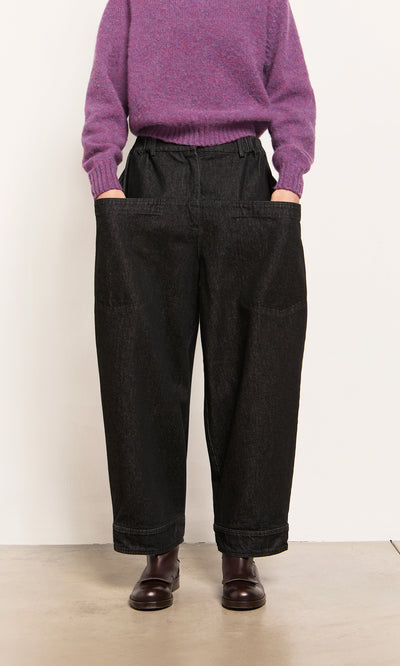 Plümo  Person in a purple sweater, Polder Pants - Washed Black with elastic waist, and dark shoes.