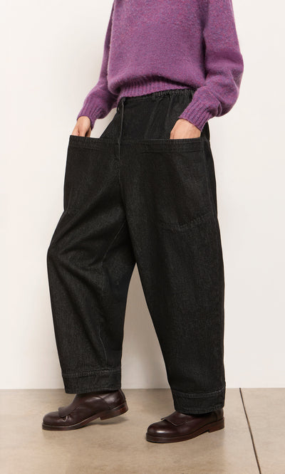 Plümo  Person in a purple sweater and Polder Pants - Washed Black with hands in pockets, wearing dark brown shoes.