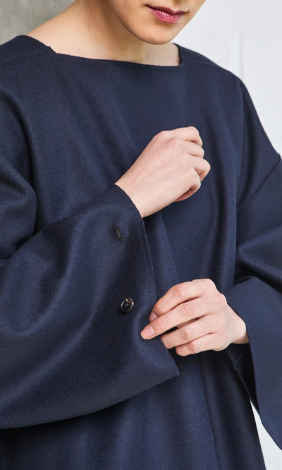 Plümo- Person wearing a loose Porter Wool Top in navy, adjusting the sleeve with their hands, face partially visible.