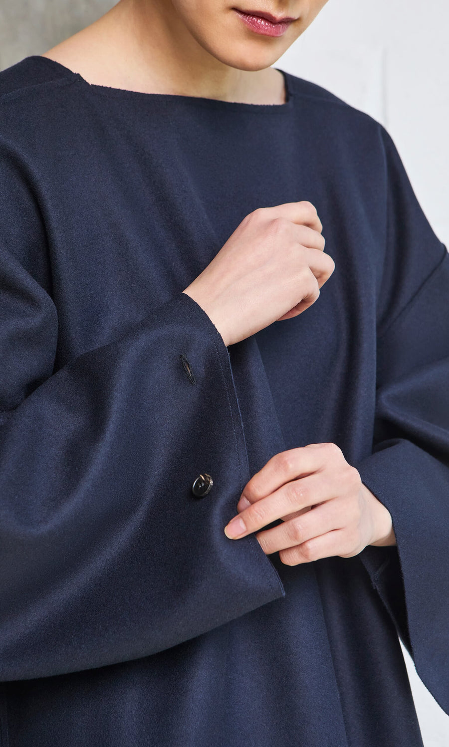 Plümo- Person wearing a loose Porter Wool Top in navy, adjusting the sleeve with their hands, face partially visible.