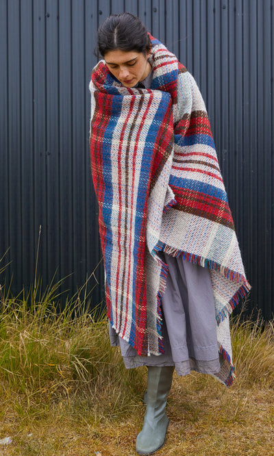 Plümo  A person wrapped in a red, blue, and white Random Throw with fringed edges.