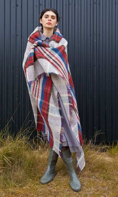 Plümo  Person wrapped in a Random Throw featuring a red, blue, and cream plaid pattern with frayed edges.