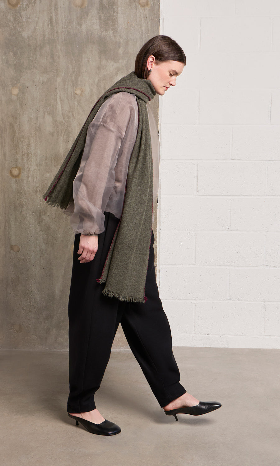 Plümo  A person in a sheer top, black pants, and heels walks indoors, accessorized with a Cashmere Wrap.