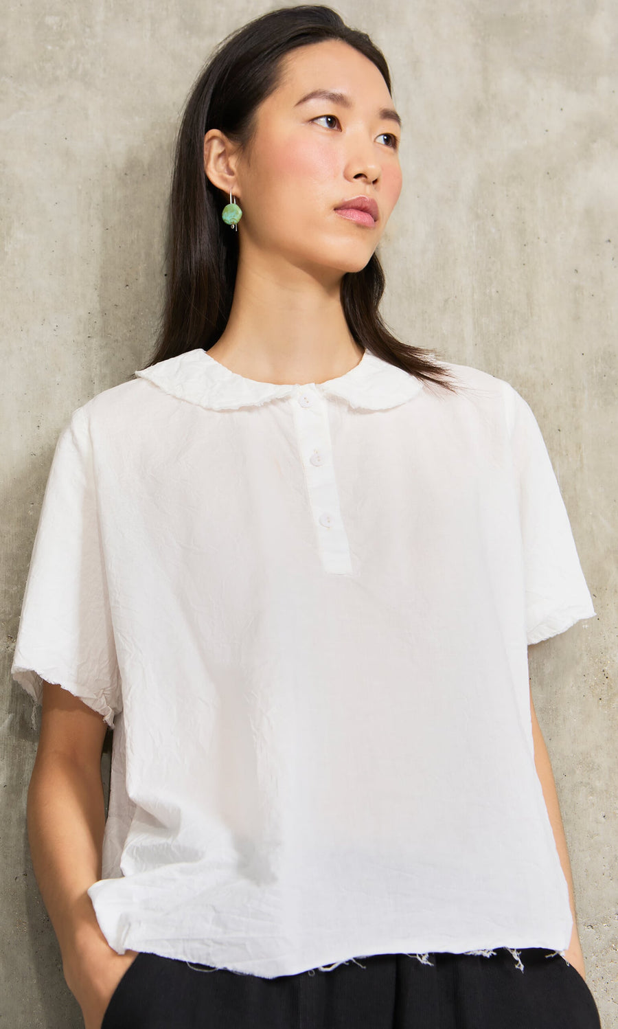 Plümo- Woman in a short-sleeve white blouse wearing Erika Earrings, handcrafted marbled turquoise resin, by a concrete wall.