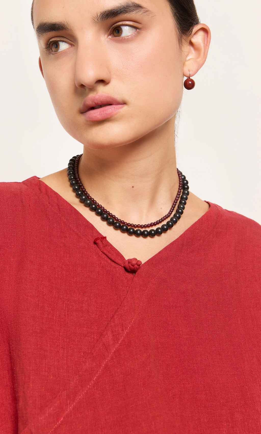 Plümo  Woman in a red top wears the Rowena Necklace and a matching red earring, gazing to the side.
