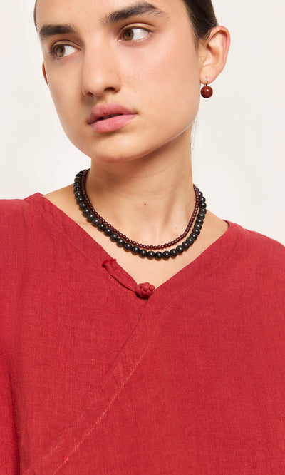 Plümo  Woman in a red top wears the Rowena Necklace and a matching red earring, gazing to the side.