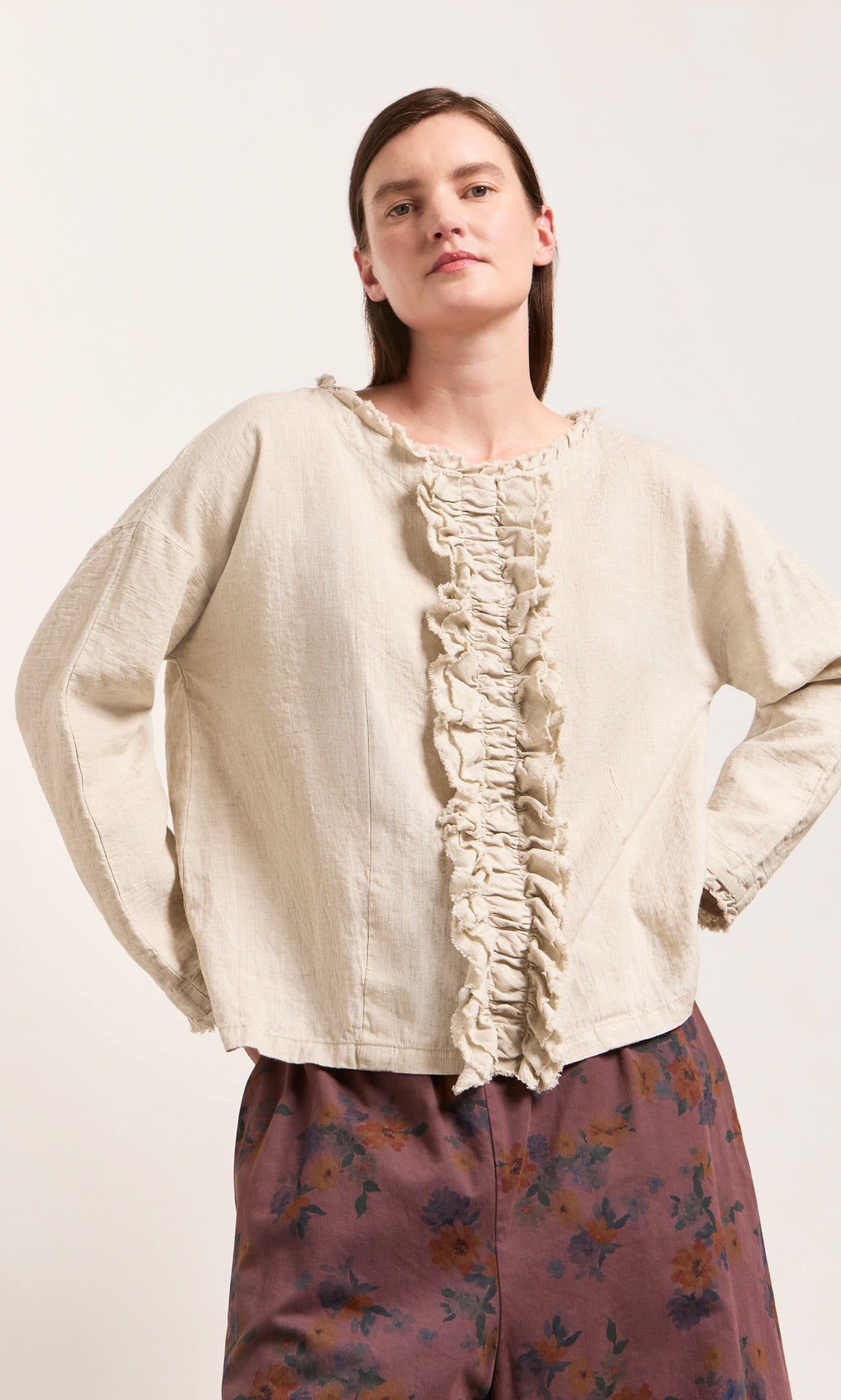 Plümo  Person in an Ella Ruffle Top and burgundy floral pants stands with hands on hips against a plain background.