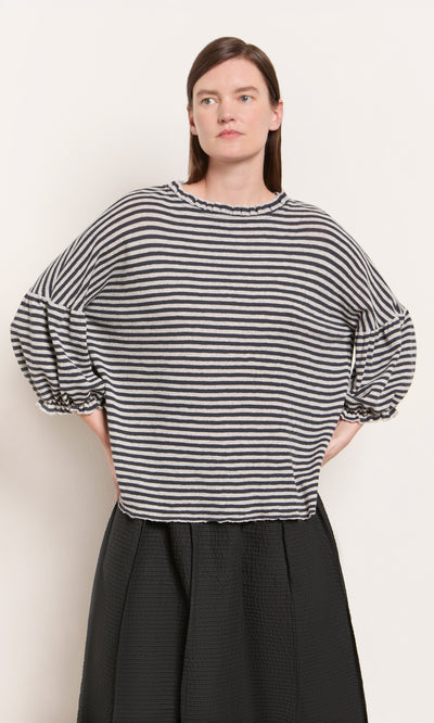 Plümo  A woman wears the Ruffle Top - Dawn Grey with voluminous sleeves and a black skirt against a light background.
