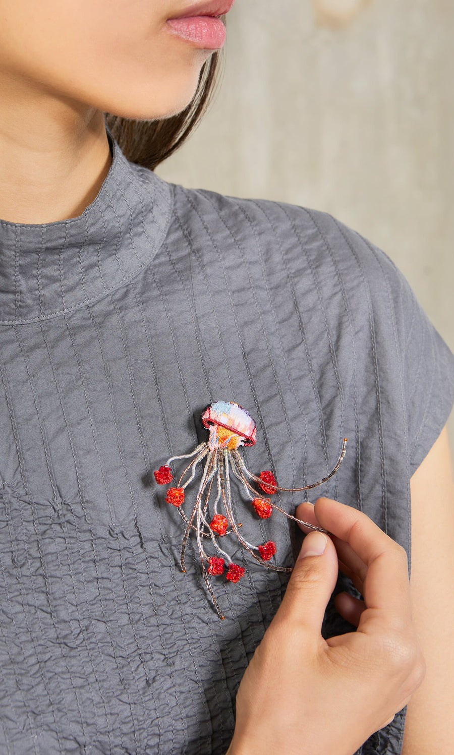 Plümo- A woman wears a textured gray top and a Sea Nettle Brooch with red accents on her chest.