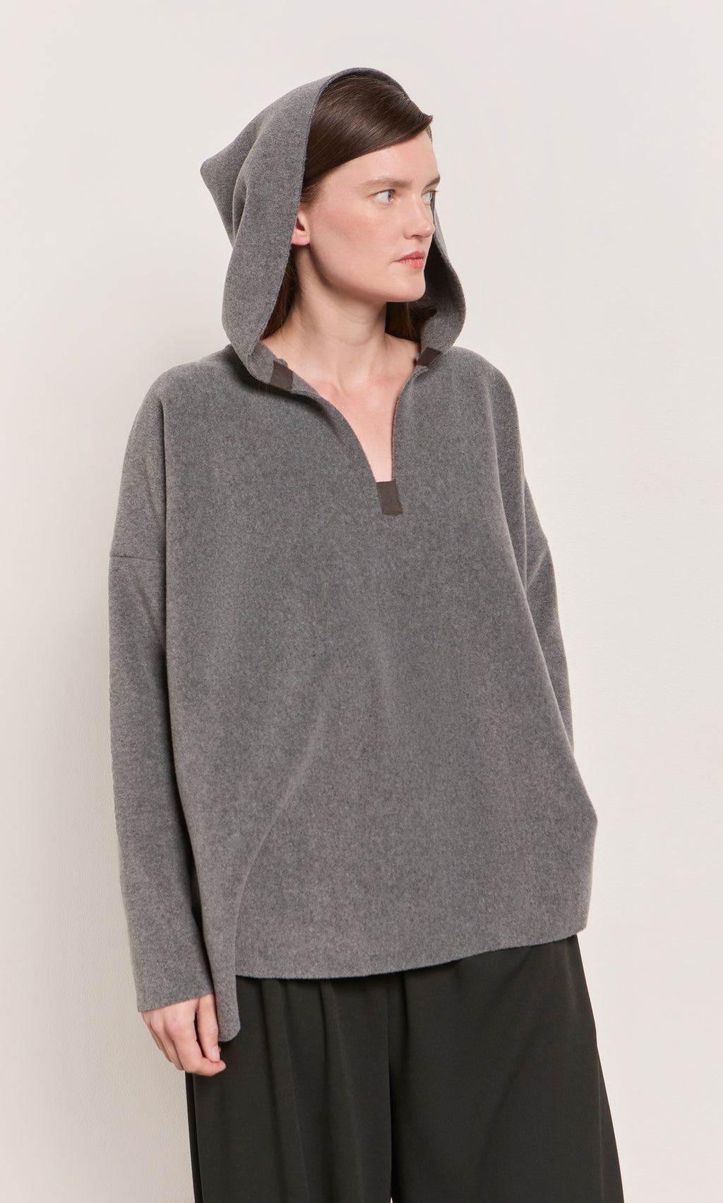 Plümo  Woman in a Grey Felted Hoodie stands against a plain light background, looking aside.