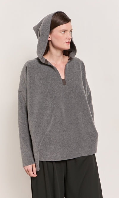 Plümo  Woman in a Grey Felted Hoodie stands against a plain light background, looking aside.
