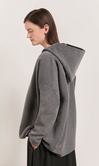 Plümo  Model wears the Grey Felted Hoodie, standing sideways with hands in pockets against a plain background.
