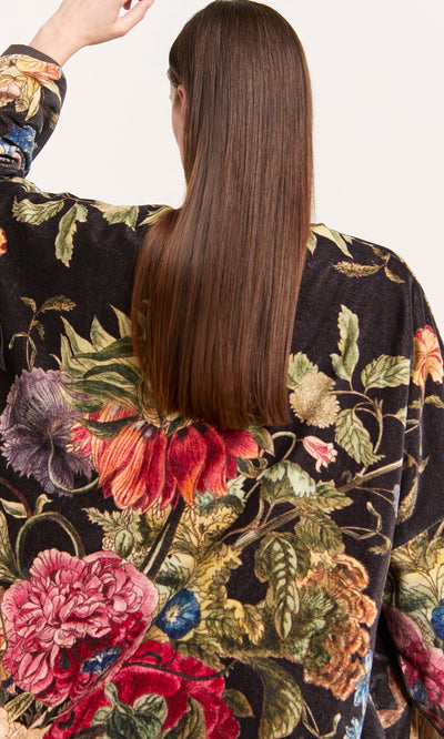 Plümo  Person with long, straight brown hair wears a Shilling Velvet Coat, raising one arm, seen from behind.