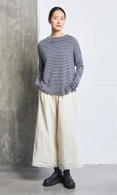 Plümo- Person wearing the Silvi Mockneck (dark navy stripe), wide cream pants, and black boots against a concrete wall.