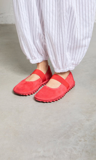 Plümo- Person wearing loose white pants with thin black stripes and Sola Red Flats on a concrete floor.