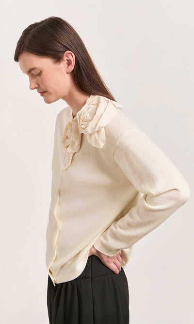 Plümo  Woman in Sugared Corsage Cardigan with sculptural shoulder corsages, standing sideways, hands on hips.