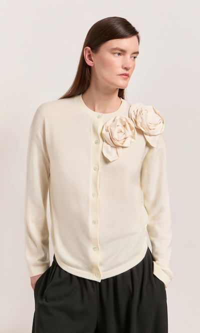 Plümo  Woman in the Sugared Corsage Cardigan in ecru with sculptural corsages on the shoulder, paired with black pants.