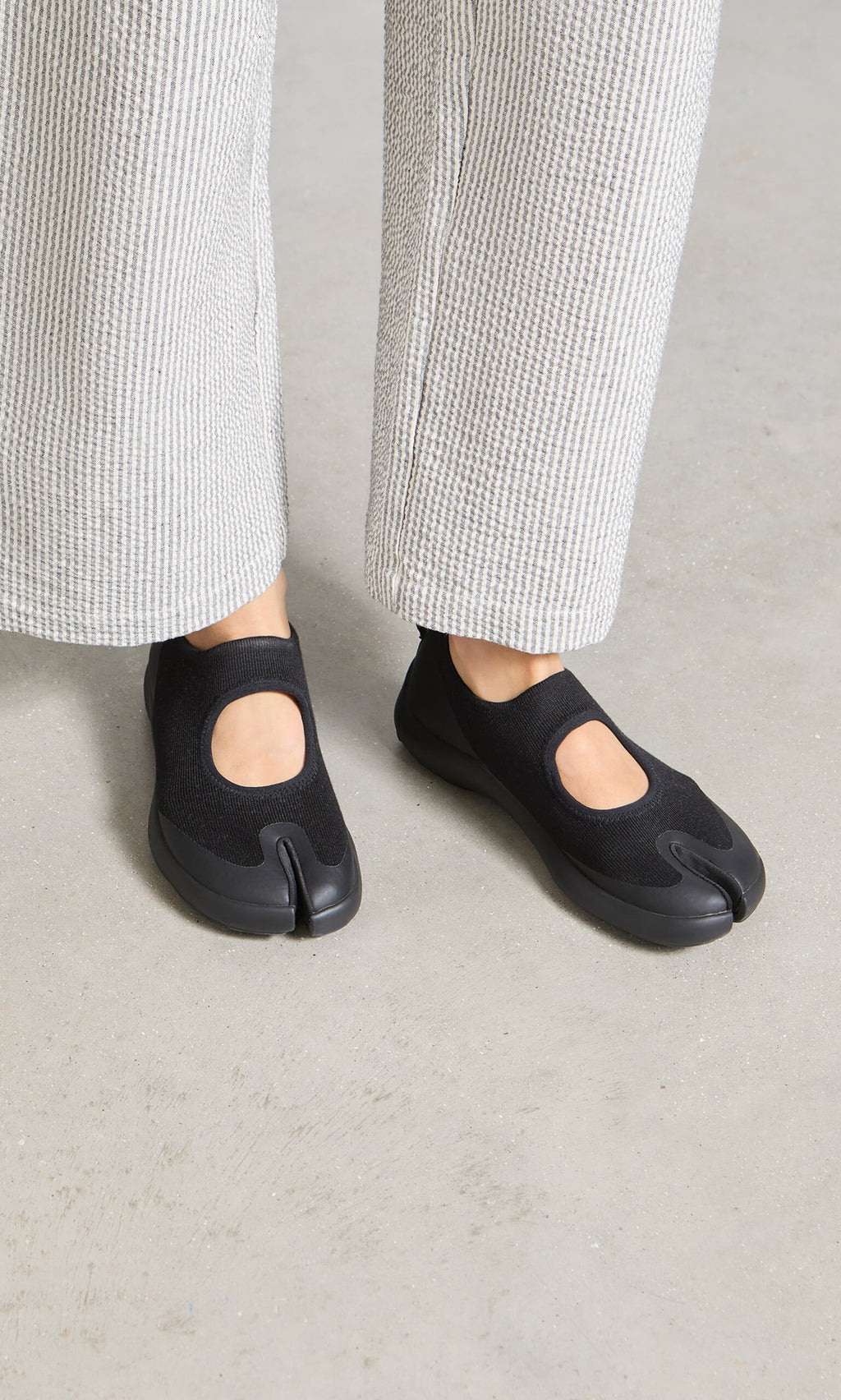 Plümo- Person wearing Tabi Sandals and light textured pants stands on a light-colored floor.