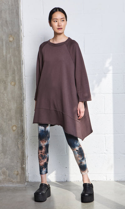 Plümo- Woman stands indoors in a relaxed fit Kelie Sweater, tie-dye leggings, and black platform shoes against a white wall.