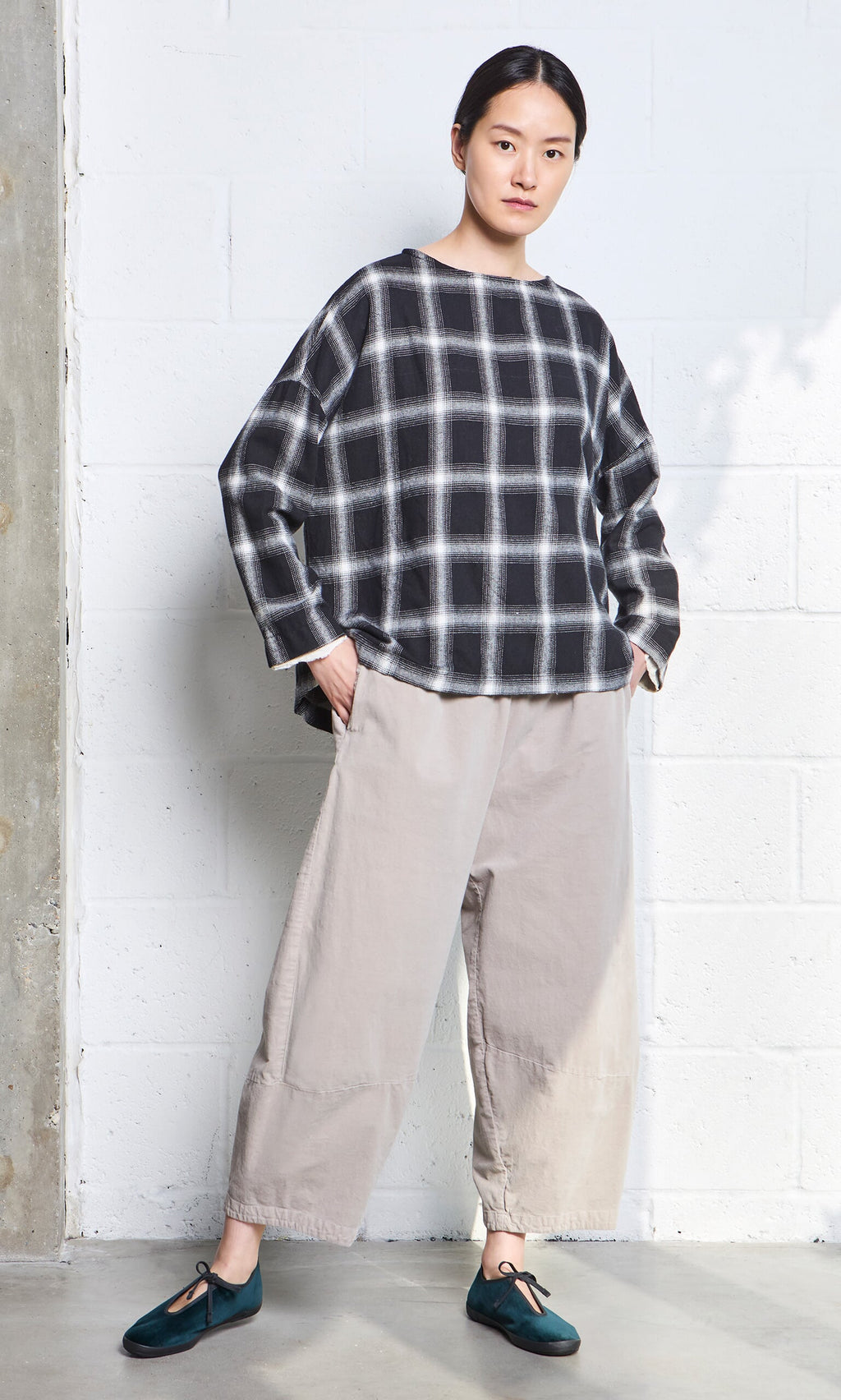 Plümo- Person wearing a black-and-white plaid top, loose beige pants, and Velvet Prim Ballerinas stands against a white wall.