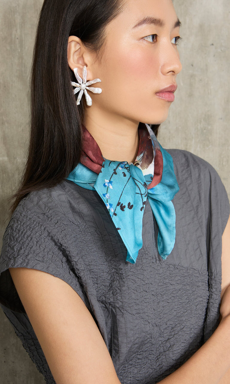Plümo- Woman in gray textured top, Ultramarine Necktie, and floral earrings, shown in a sideways pose.