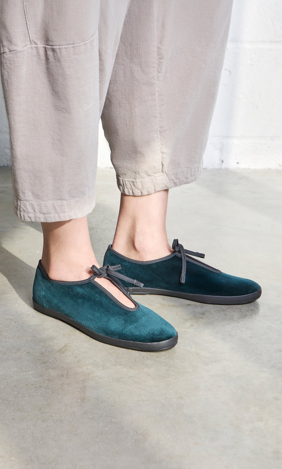 Plümo- Person in teal Velvet Prim Ballerinas with black soles and ankle-length beige pants, standing on concrete.