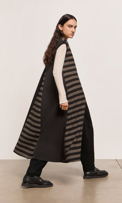 Plümo  Person in a Venlo Stripe Tunic, cream long sleeve shirt, black pants, and black shoes walking indoors.