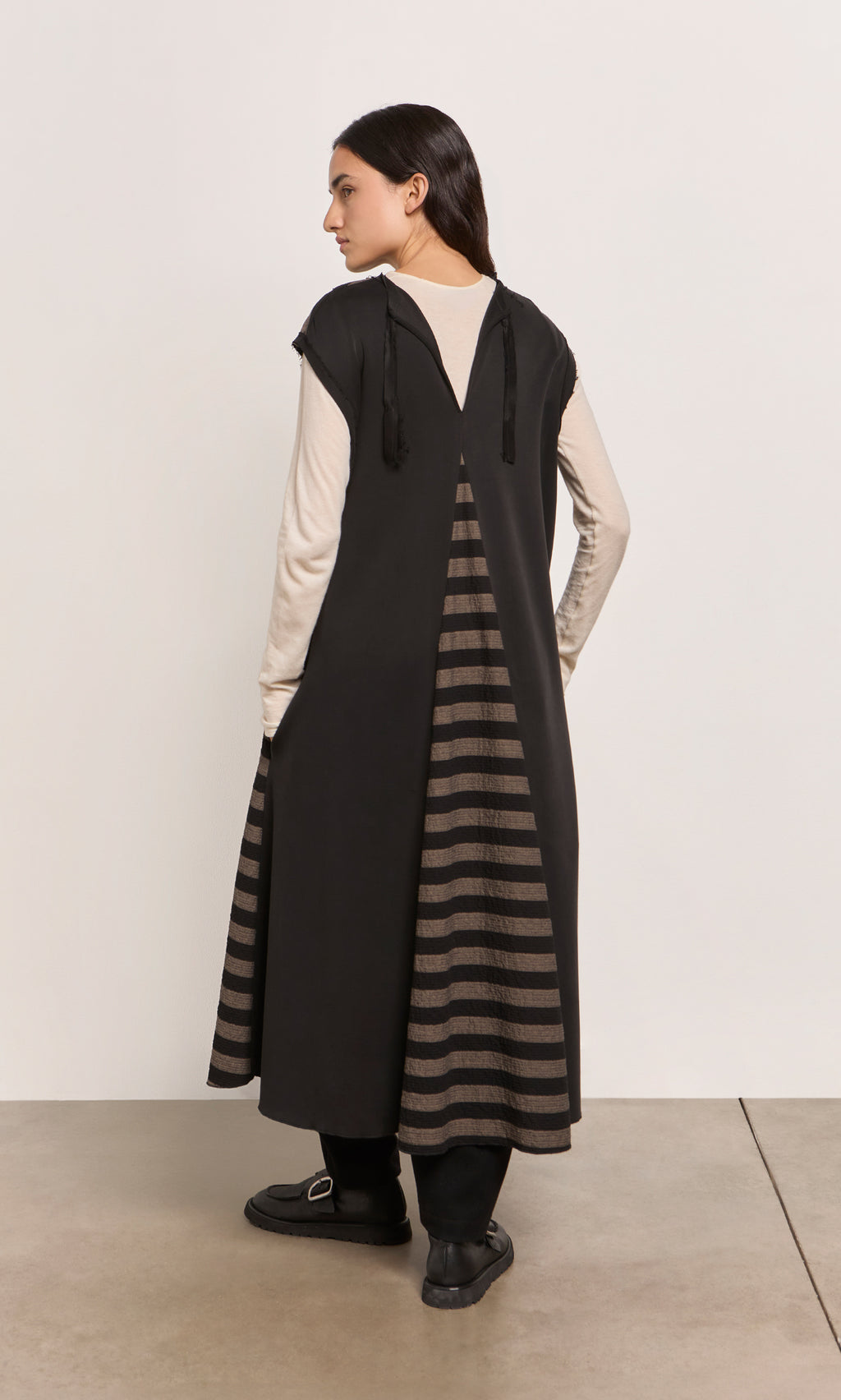 Plümo  A woman stands sideways in the Venlo Stripe Tunic, layered over a cream top for a contrasting look.