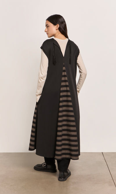 Plümo  A woman stands sideways in the Venlo Stripe Tunic, layered over a cream top for a contrasting look.