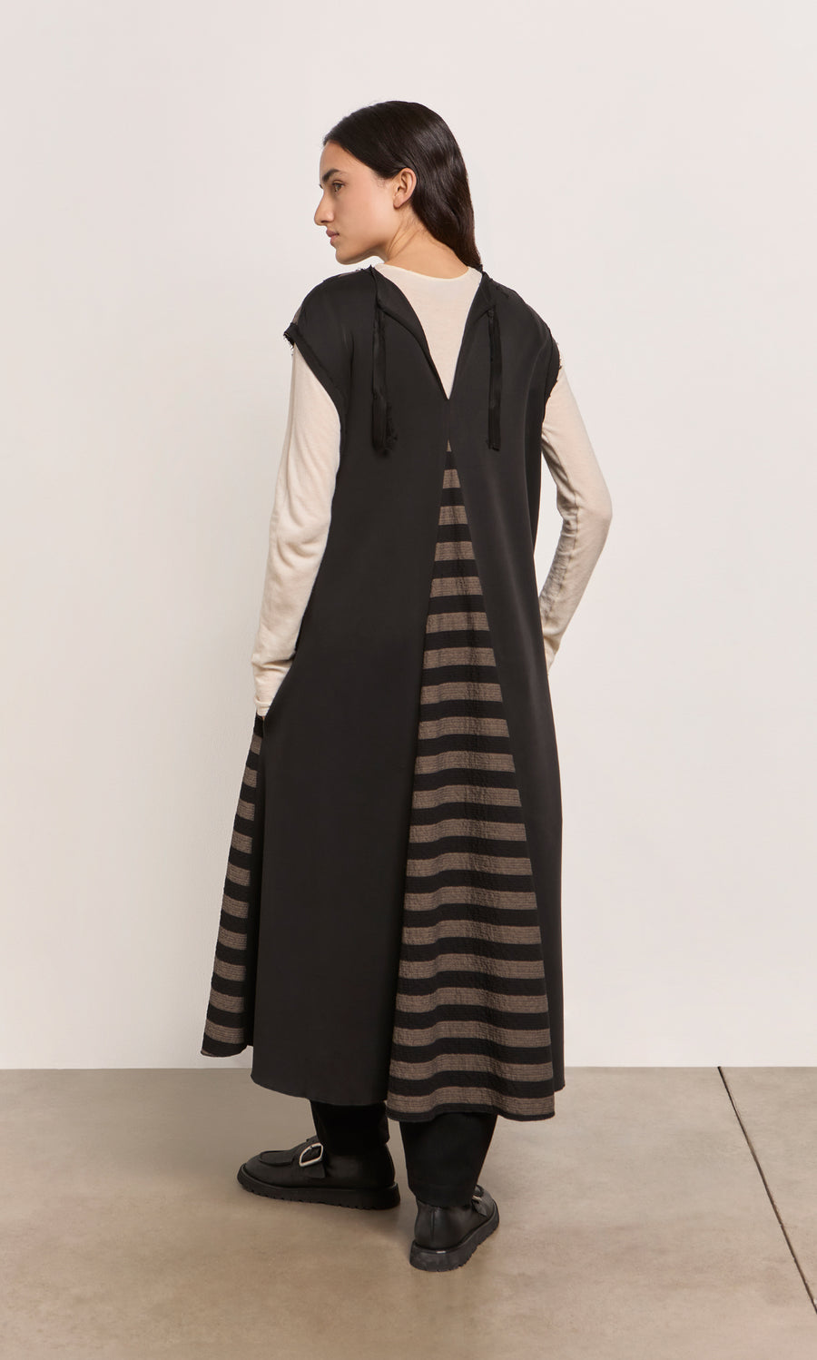 Plümo  A woman stands sideways in the Venlo Stripe Tunic, layered over a cream top for a contrasting look.