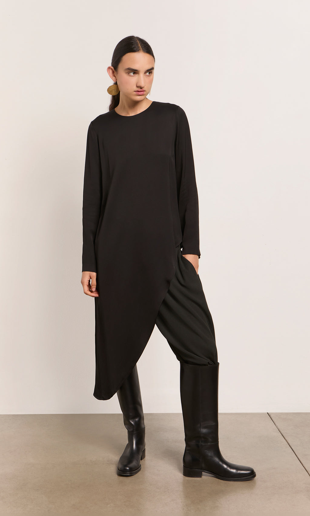 Plümo  Model in the Vermeer Top, black pants, and tall boots stands against a plain background.