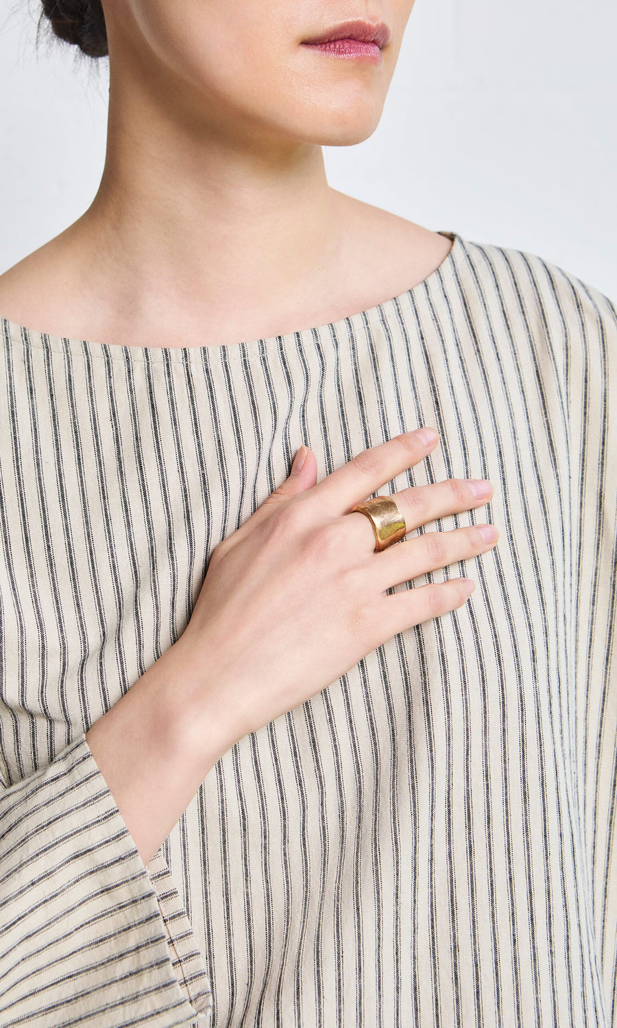 Plümo- A woman in a striped shirt rests her hand with the Vinci Ring on her chest, visible from shoulders to lips.