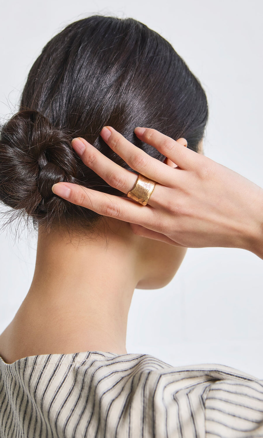 Plümo- Woman with dark hair in a low bun, wearing the handmade Vinci Ring and a striped top, hand raised near her head.