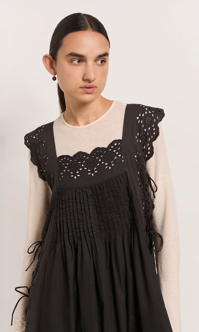 Plümo  Woman in a Vintage Lace Dress over a cream top, looking to the side against a plain backdrop.