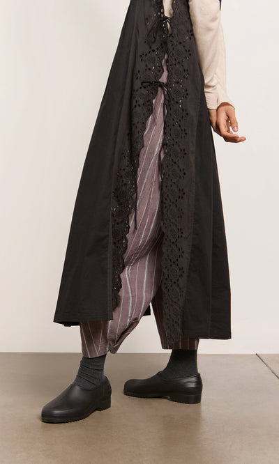 Plümo  Person wearing a Vintage Lace Dress and striped pants with black shoes, standing on a gray floor.