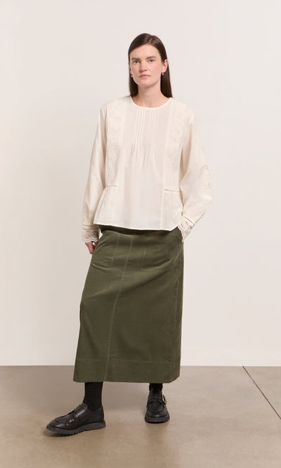 Plümo  Woman in cream blouse and Beetle Green Skirt stands against a plain background.