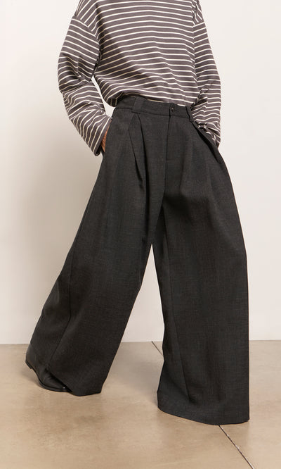 Plümo  Person in a striped long-sleeve shirt and Pleated Grey Pants, standing on a light-colored floor.