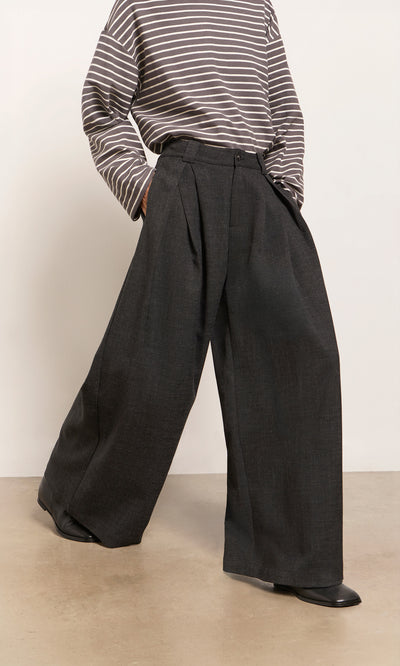 Plümo  Person wearing Pleated Grey Pants, black shoes, and a gray striped long-sleeve shirt while standing indoors.