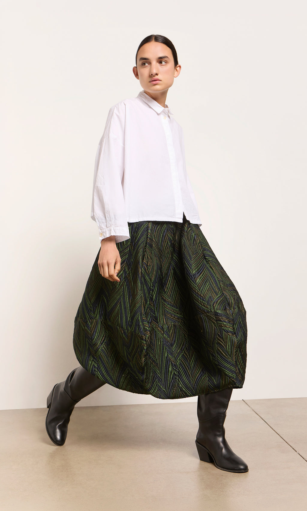 Plümo  A model in a white shirt, Yona Skirt, and black boots stands against a white background.