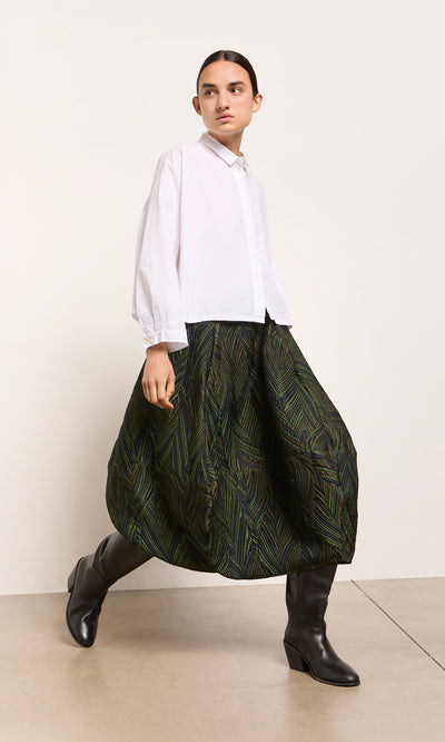 Plümo  A model in a white shirt, Yona Skirt, and black boots stands against a white background.
