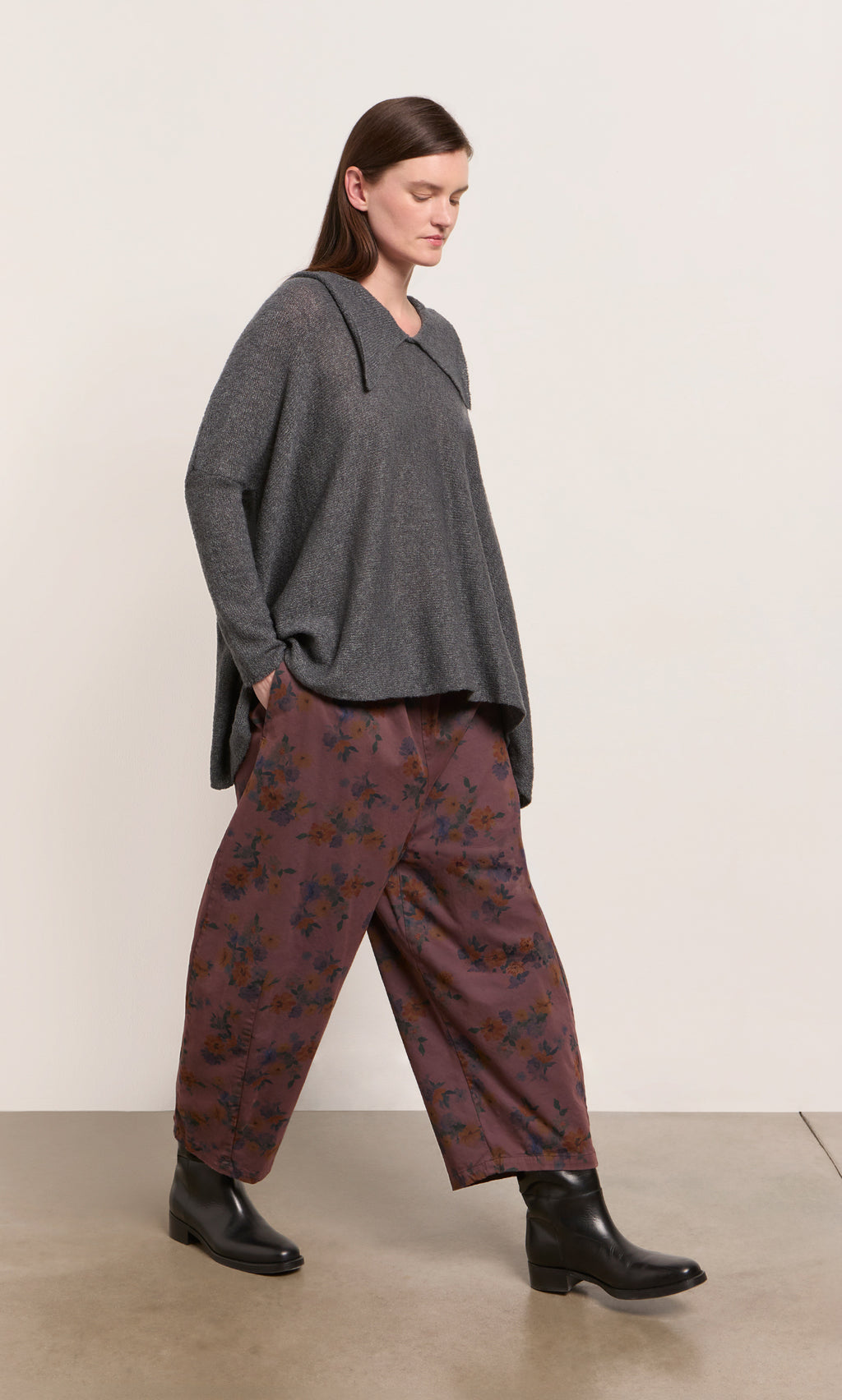 Plümo  Person in a gray sweater pairs Espel Pants with chic black ankle boots while walking indoors.